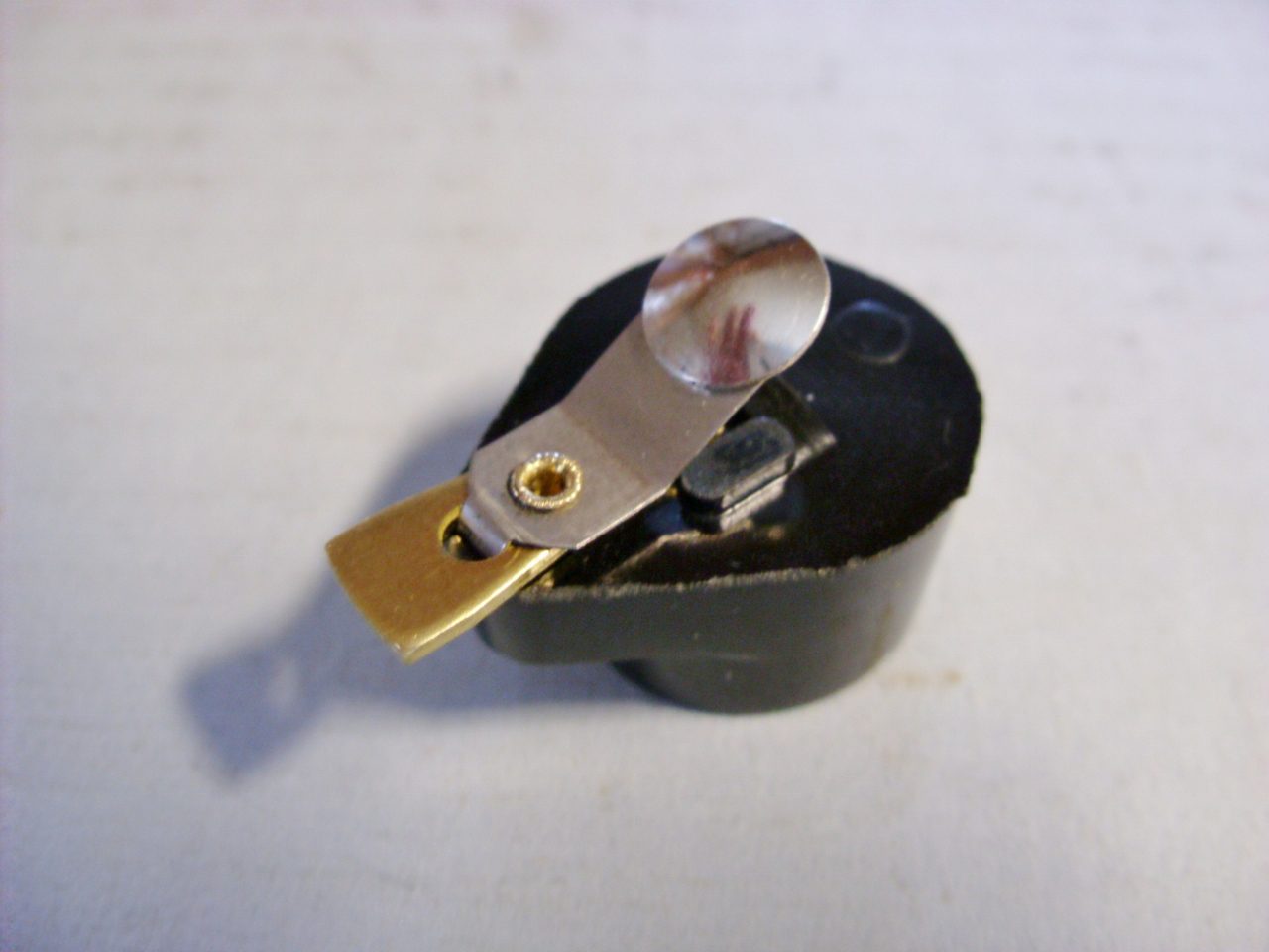 A small black and gold 1920s-50s Delco Remy style distributor rotor on a white surface.